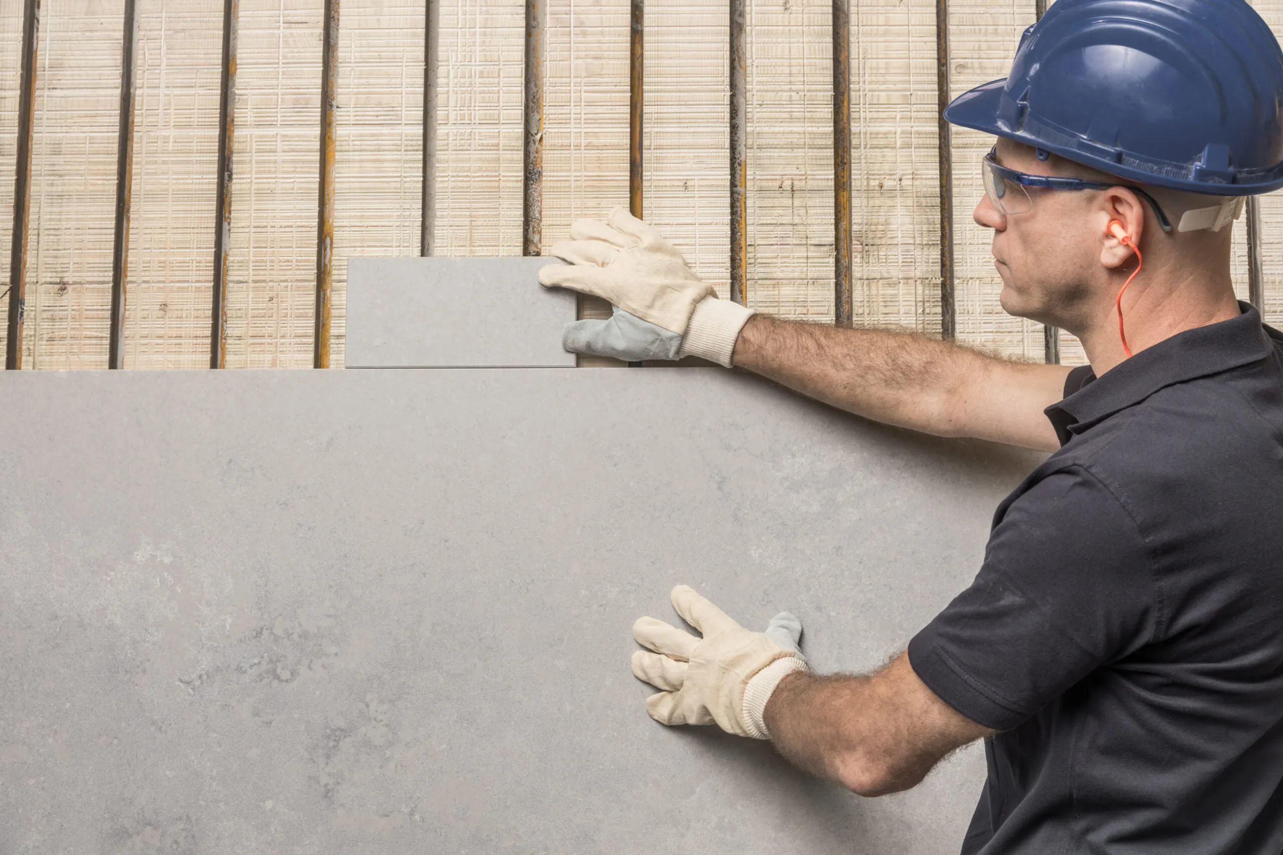 מתקין עם קסדה וכפפות בוחן לוח פורצלן גדול של אבן קיסר לפני התקנה על קיר.