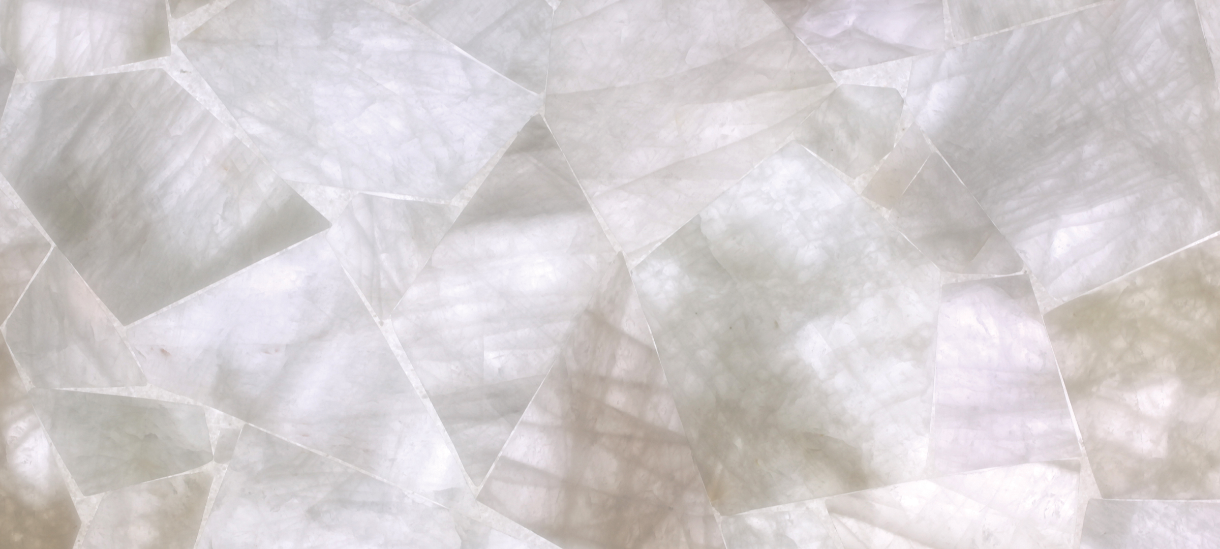 תקריב של משטח אבן קיסר במראה אוניקס בהיר, עם דוגמת לוחות חצי־שקופים בגווני לבן ואפור, המדגישים עומק ומרקם טבעי.