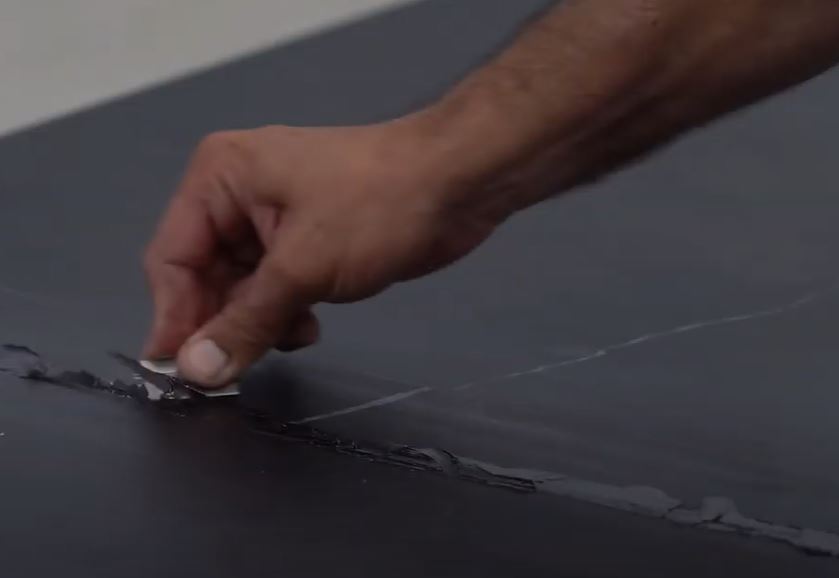 עובד במפעל קוורץ מכין חומר בעזרת בקבוק סחיטה, כשהוא לובש חולצת עבודה של Caesarstone וברקע ציוד תעשייתי ולוחות קוורץ מסודרים