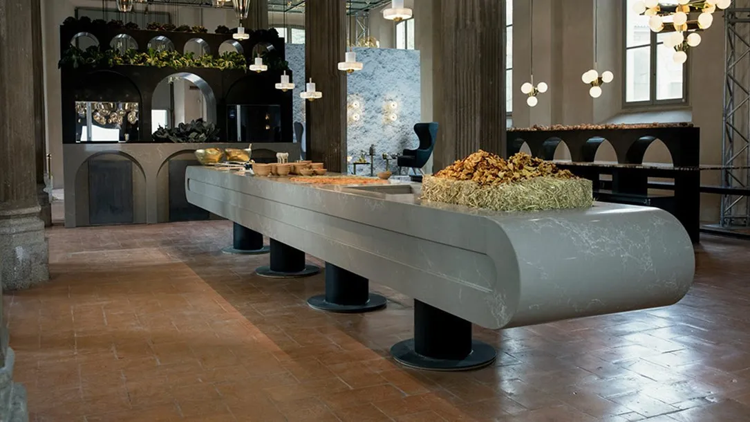 דלפק תצוגה ארוך בעיצוב ייחודי מאבן קיסר עם קימור בקצוות, מוצב על בסיסים גליליים בחלל תעשייתי מהודר.